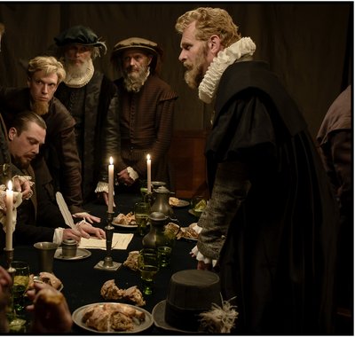 Mannen staan rondom een tafel. Ze dragen 17de eeuwse kleding. Er wordt een document ondertekend met een veren pen.