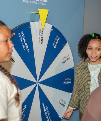 Een groepje kinderen staat rondom een wiel met stellingen waaraan gedraaid kan worden.