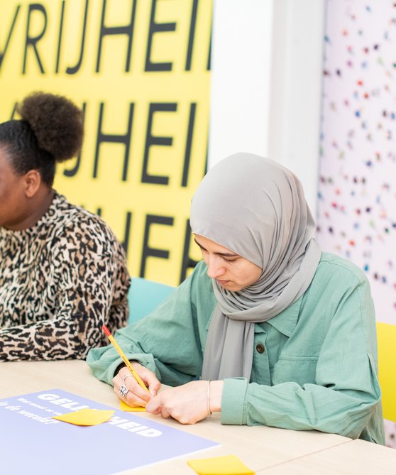 Kinderen zitten aan een tafel in Hof van Nederland en zijn aan het werk.