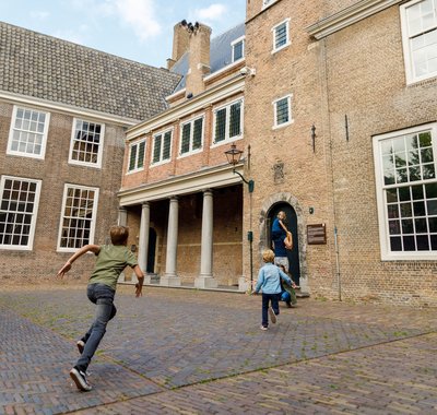 Rennende kinderen op het Hofplein van Hof van Nederland. Een volwassene staat met een kind op zijn schouders op ze te wachten.