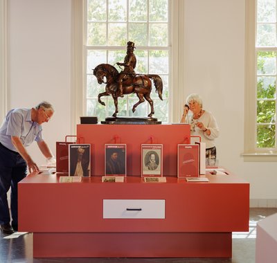 Twee oudere mensen in een zaal van het museum. De man kijkt naar een voorwerp, de vrouw luistert.