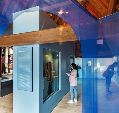 In een voornamelijk blauwe museumzaal bekijken een man en vrouw de voorwerpen en schilderijen.