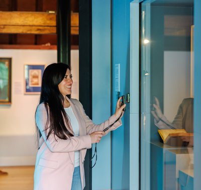 In een voornamelijk blauwe museumzaal bekijken een man en vrouw de voorwerpen en schilderijen. De vrouw drukt op een knopje om te kunnen luisteren.