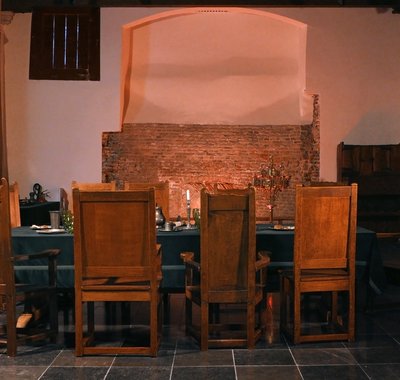 Zaal zonder mensen. Er staat een tafel met stoelen er om heen. Er brandt een kaars op tafel.