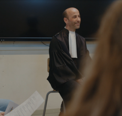 Man in toga zit voor een groep leerlingen.