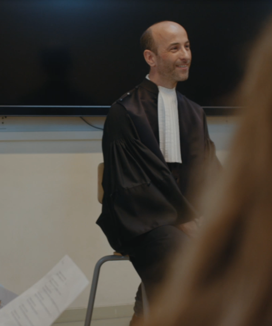 Man in toga zit voor een groep leerlingen.