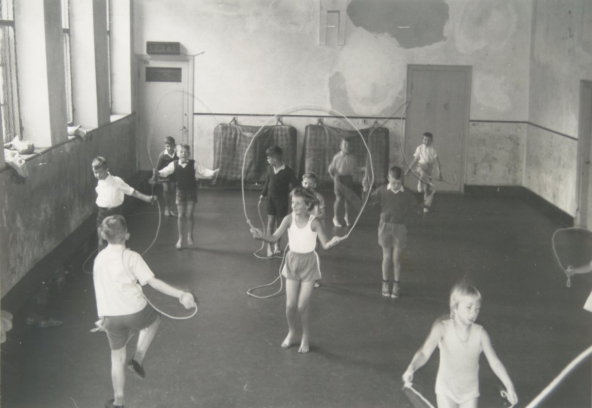 Kinderen in gymkleding zijn aan het gymmen. Ze gebruiken touwen.