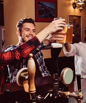 Drie vrienden waaronder een man en twee vrouwen, proosten met bier in een pub.