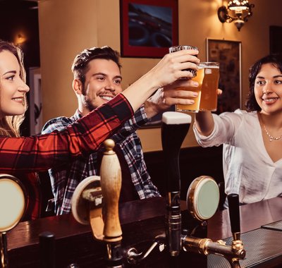 Drie vrienden waaronder een man en twee vrouwen, proosten met bier in een pub.