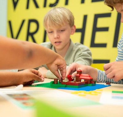 Kinderen zitten aan een tafel en maken met lego een middeleeuwse stad na